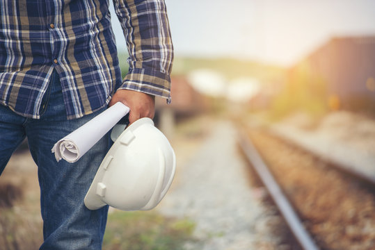 Construction Worker Concept.Civil Engineer Holding Safety Hard Hat And Blue Print At Train Station Background,Worker,Foreman Or Safety Officer Inspect And Work At Construction Site.