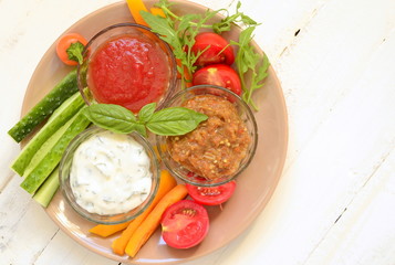 Plate with three healthy different dips and vegetables, top view