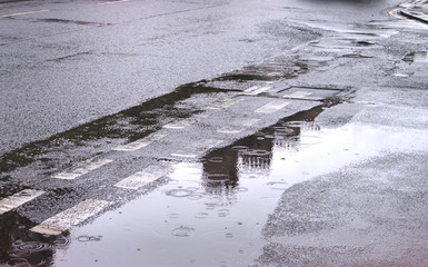 A photograph of the reflection in the water of chimney stacks from a tenement building in Edinburgh in large puddles on a road following storms.