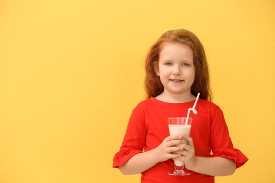 Little girl with glass of delicious milk shake on color background