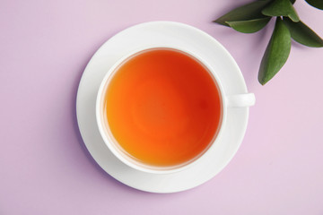 Cup of delicious tea with green leaves on color background, top view