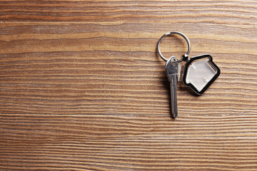 Key with trinket in shape of house on wooden background. Real estate agent services