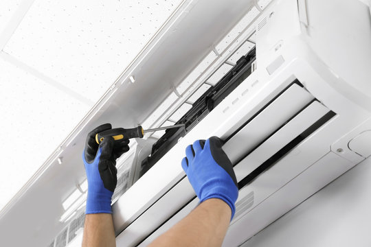 Male technician fixing modern air conditioner indoors