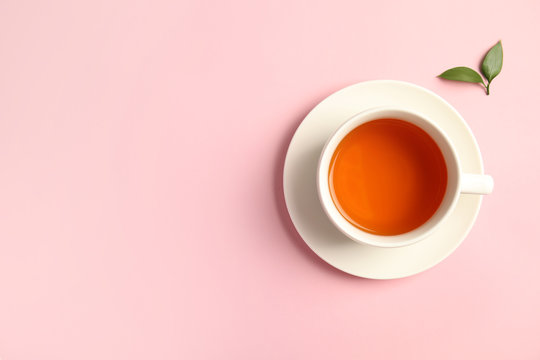 Cup of delicious tea with green leaves on color background, top view