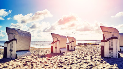 Retro stylized picture of wicker hooded basket chairs on a beach at sunset, summer holidays concept.