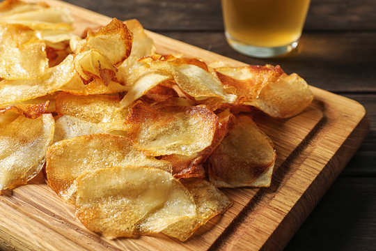 Wooden board with crispy potato chips on table, closeup