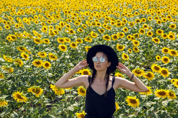 young sexy girl in black dress and hat in field with yellow sunflowers