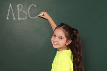 Little school child writing with chalk on blackboard