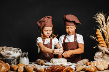 Adorable girl with brother in chief hats and aprons cooking at table with bread loaves making fresh...