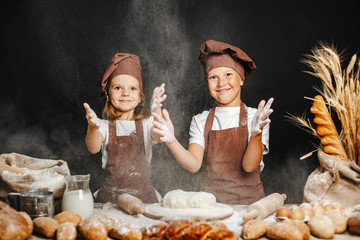 Adorable girl with brother in chief hats and aprons cooking at table with bread loaves making fresh...