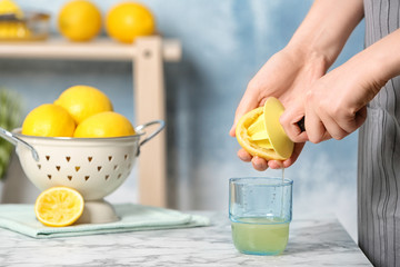 Woman squeezing lemon juice with reamer into glass on table