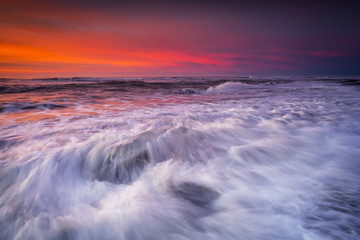 Jokulsarlon beach at sunrise, long exposure photography with waves and pieces of ice on the black sand beach.