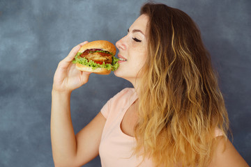 Pleasure, delight, enjoyment, treat, happiness, appetite, fast food. Cute young woman eating greedily delicious burger enjoying its taste