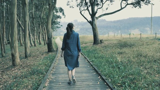 4k pretty young girl walking on the natural wooden podium in the beautiful nature grove with green hills on the background
