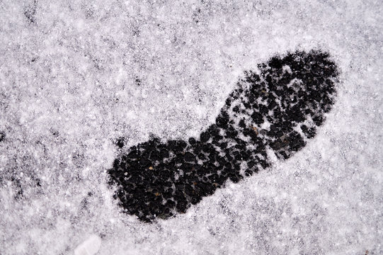 Shoe footprint in snow on winter asphalt road