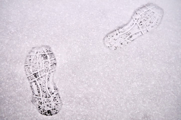 Shoe footprints in snow on winter asphalt road