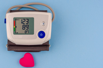 Modern electronic blood pressure monitor with red heart on a blue background.