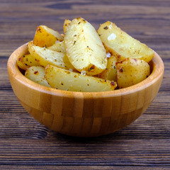 Roasted potatoes with provence herbs and salt in bowl on wooden background. Close up view.