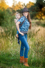 Fototapeta premium Cowgirl mother carrying her small daughter in a baby sling