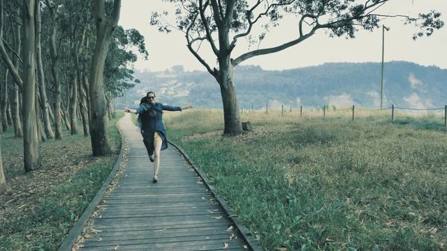 4k pretty young girl walking on the natural wooden podium in the beautiful nature grove with green hills on the background