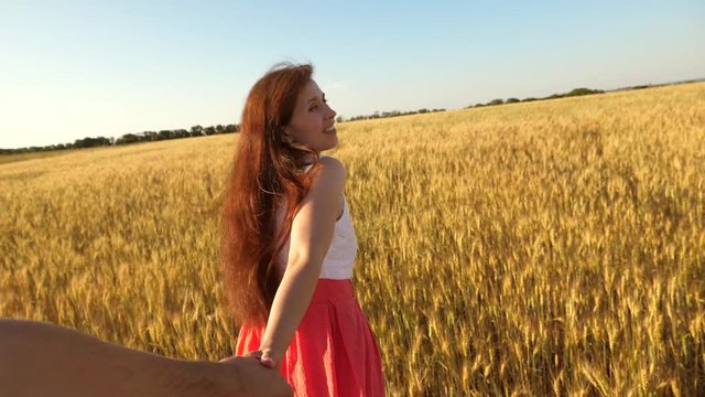 Girl with long hair runs across field with wheat holding loved one hand and laughs and looks back at him. Slow motion.