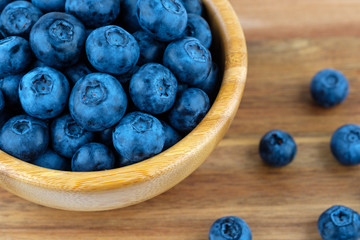 Ripe blueberries in wooden bowl on wood table background. Side view.