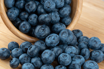 Ripe blueberries in wooden bowl on wood table background. Side view.
