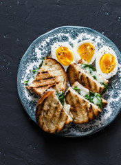 Delicious snack - boiled eggs and spinach grilled cheese sandwiches on dark background, top view