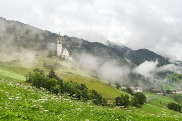 Church on a misty hillside with a cloudy valley in the background in the Dolomites mountains in La Valle, South Tyrol, Italy	
