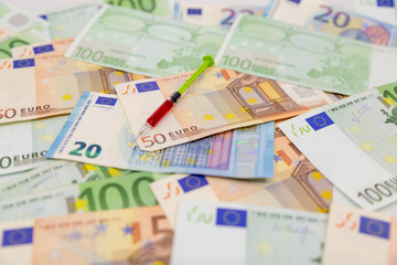 Spread Stack of Euro Banknotes with syringe on top of them, health costs concept