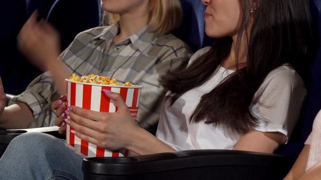 Cropped sliding shot of three young cheerful women enjoying watching comedy movie at the local cinema. Female friends relaxing at the movie theatre. Teenagers, weekend concept.
