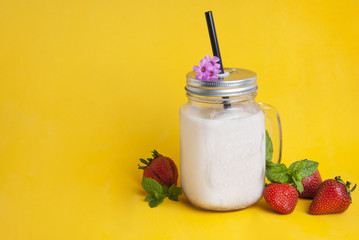 Healthy strawberry smoothie or drink yogurt in a mason a jar glass with berries and mint, over yellow background with copy space.