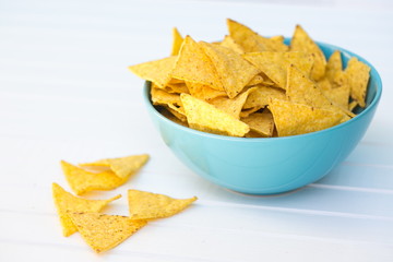 Yellow triangle shaped crispy nachos in a blue turquoise bowl placed on white table, copy space,...