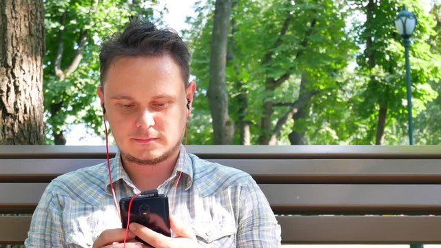 Handsome young man wears red music headphones, listening to music and changes audio tracks on smartphone