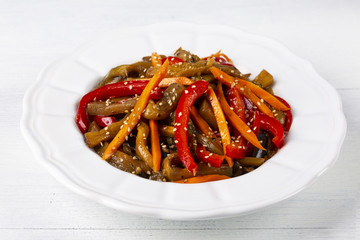 Vegetable salad. Aubergines fried, pepper, carrots on a white plate. The concept of healthy eating. White wooden background.