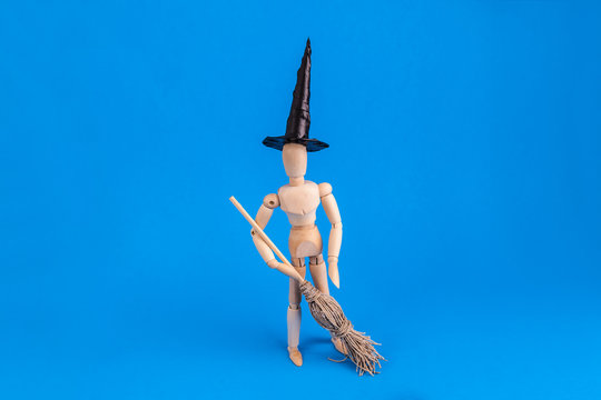Halloween witch wooden jointed manikin doll holding broom wearing a black witch hat on blue background
