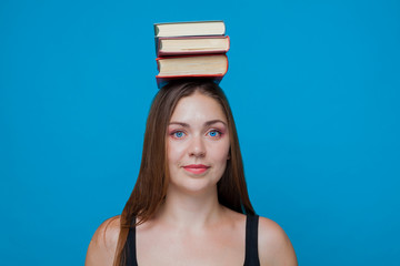 Young pretty woman with 3 books on her head, smilin; wearing black blouse. Cropped from chest line; on the blue background, isolate, centred