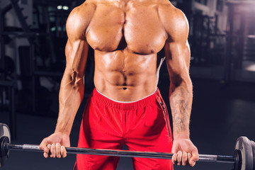 Fototapeta premium Close up of muscular young man lifting weights in gym