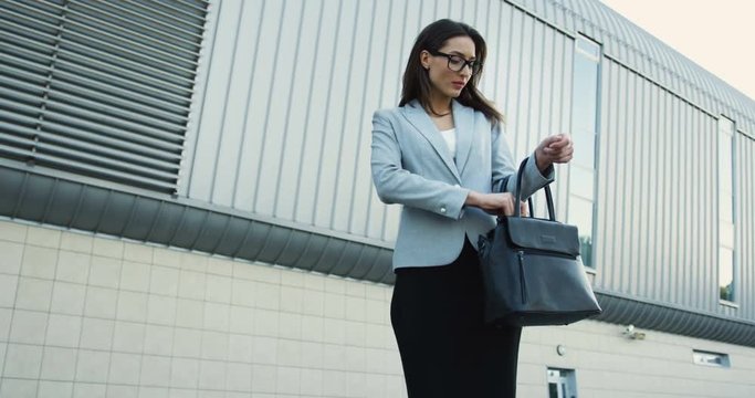 Caucasian pretty woman in the glasses having her phone ringing, taking it from a baf and talking while going to work in the office.