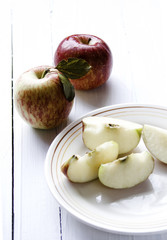 Two apples and several slices inside a porcelain dish on the white wooden table