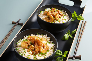Two bowls of black color with rice and fried shrimp on a blue table. Asian food.
