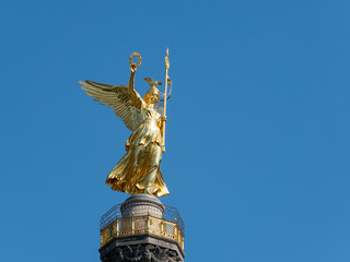 Obraz premium The Golden Statue of Victoria On Top of The Victory Column in Berlin, Germany Against A Blue Sky