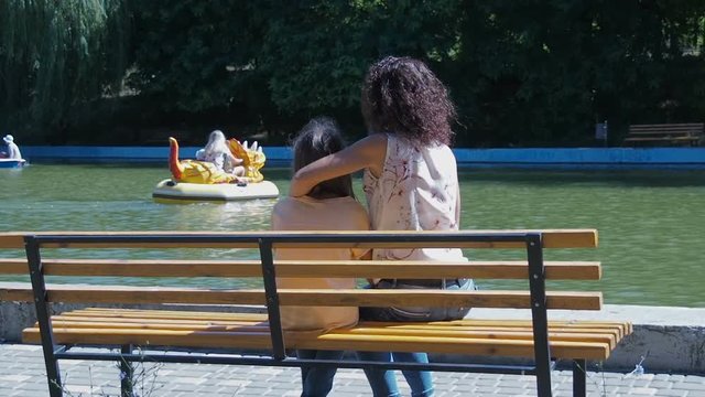 Happy family in the park. The child with mother in the park on the bench watching the water attractions.
