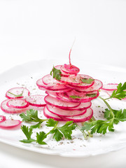 Juicy pink radish cut into a slice with herbs on a white plate