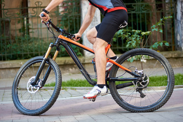 Fototapeta na wymiar Crop view of male cyclist wearing professional sportswear riding bicycle along paved streets. Close up of sport bike on city streets. Concept of healthy lifestyle, outdoor training