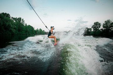 Young active girl riding on the wakesurf holding a rope of a motorboat