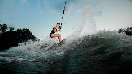 Active woman riding on the wakesurf holding a rope of a motorboat