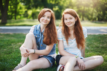 My sister is best friend. Good-looking two female with red hair and freckles, sitting on grass near...