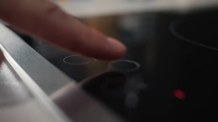 A close-up of a female hand includes an electric stove. Modern technology. Touch panel of electric cooker