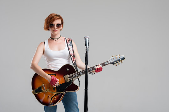 Portrait of a beautiful young rock woman in sunglasses with a guitar. She sings a song in studio microphone